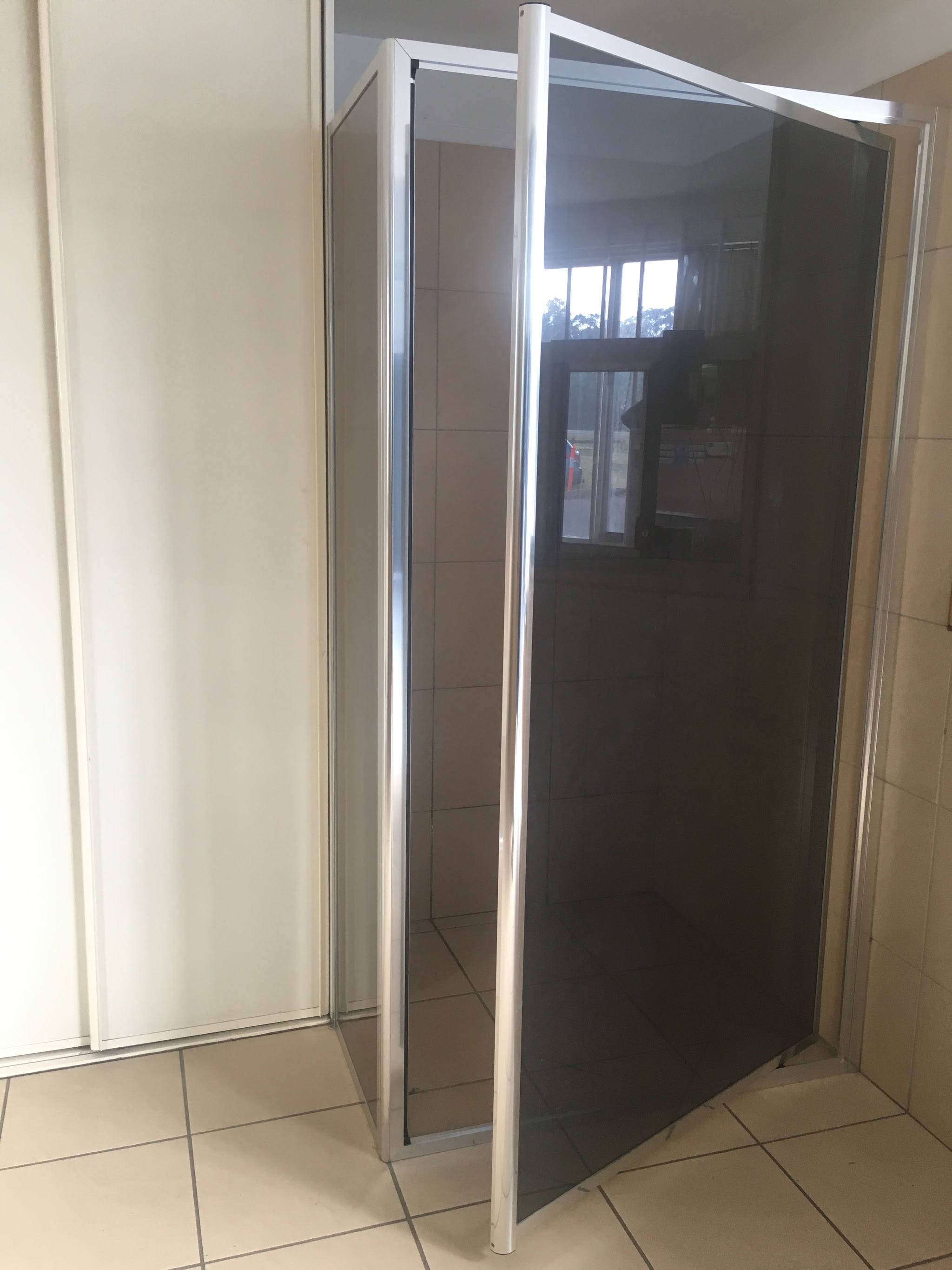 A framed pivot shower screen in smoked glass beside white sliding wardrobe doors on the showroom floor