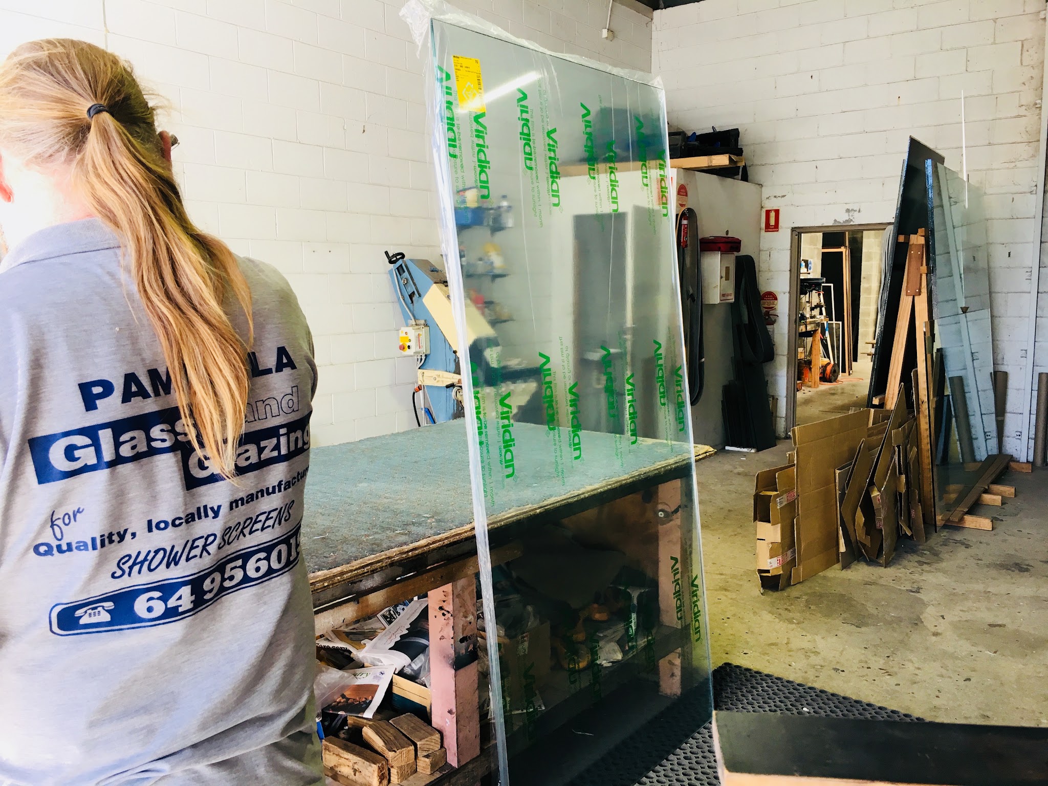 A member of the Pambula Glass team carrying a sheet of Viridian glass through the workshop, past the cutting bench