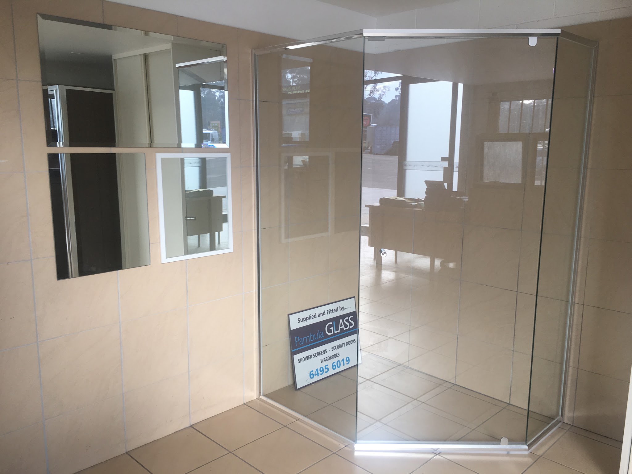 Frameless shower screen and bevelled mirrors on the tiled display wall in the Pambula Glass showroom